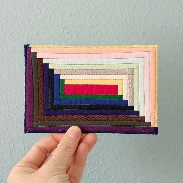 Hand holding a stack of colorful fabric swatches against a light gray background