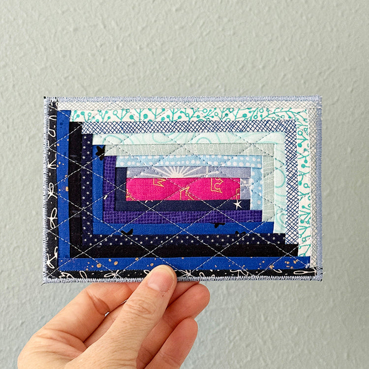 Hand holding a colorful quilted fabric card against a plain background