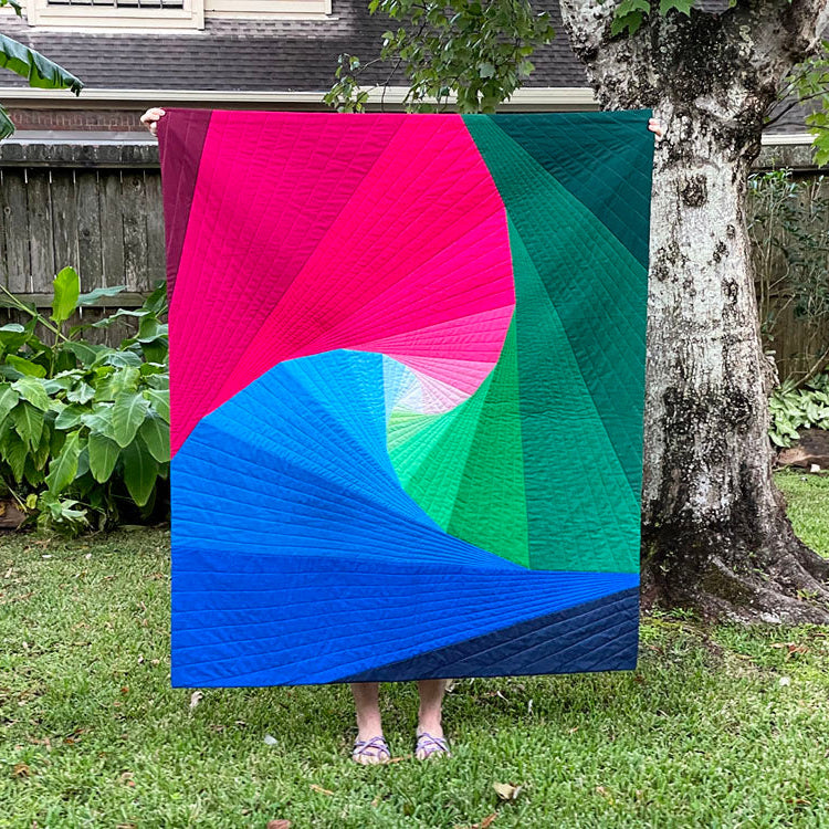 Colorful quilt with pink, green, and blue patterns draped over a person in a garden.