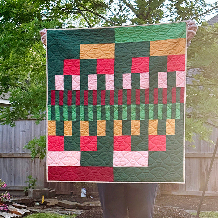 Person holding a colorful quilt with geometric pattern in an outdoor setting.